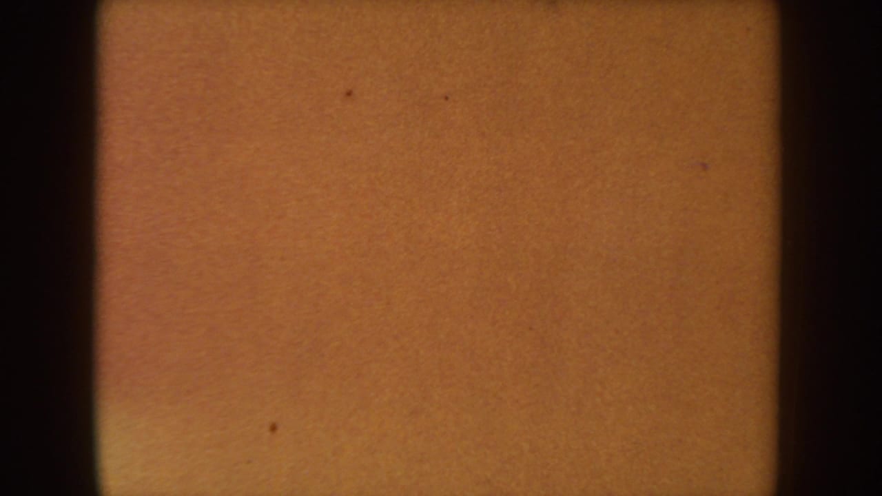 1954 South Dakota 8mm reel frame showing an amber exposed field with black gate edges, grain, and small dust marks.