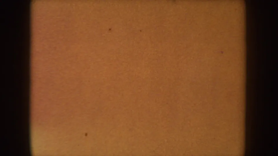 1954 South Dakota 8mm reel frame showing an amber exposed field with black gate edges, grain, and small dust marks.