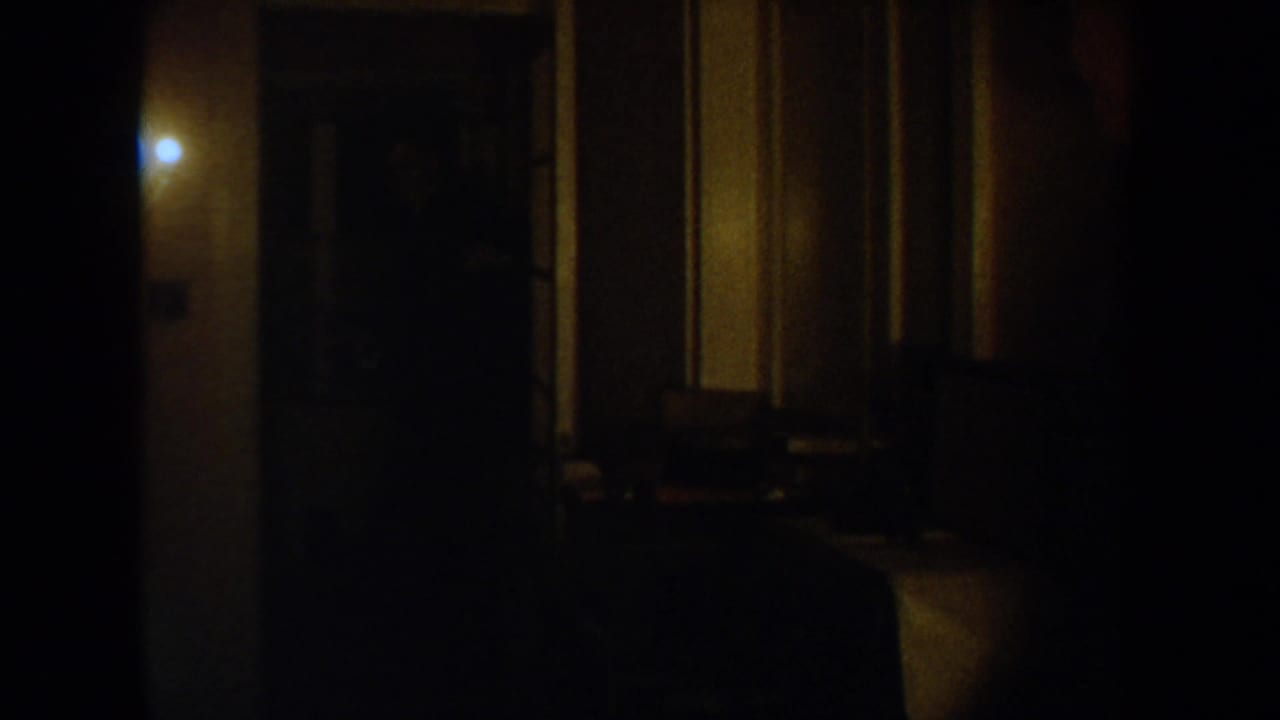 Dim 1954 South Dakota home interior with a warm wall light, dark hallway, and soft 8mm grain.