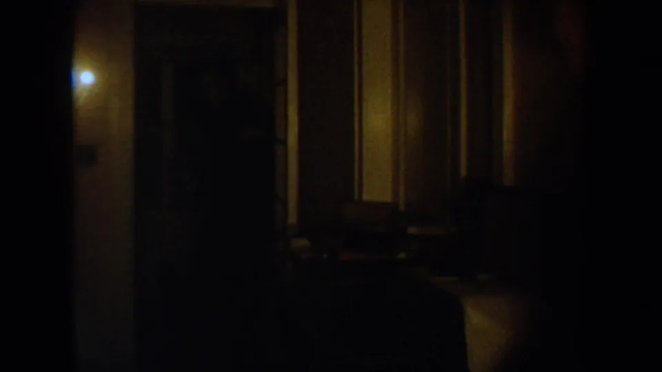 Dim 1954 South Dakota home interior with a warm wall light, dark hallway, and soft 8mm grain.