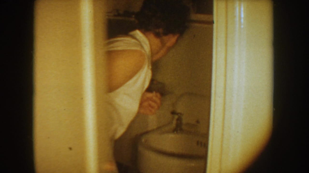 Woman in a white sleeveless top leaning over a small bathroom sink.
