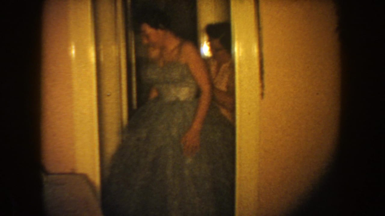 Woman in a blue formal gown leans forward beside a doorway.