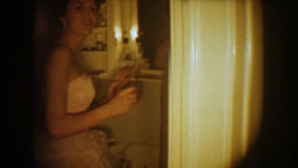 1954 South Dakota 8mm frame of the bride smiling in a bathroom while adjusting herself before the wedding.