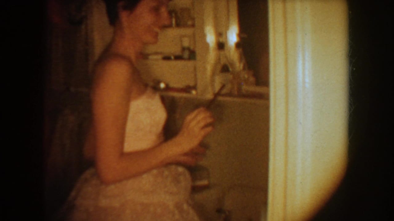 1954 South Dakota frame of a woman in a white wedding dress standing in profile inside a bathroom, with her reflection visible.