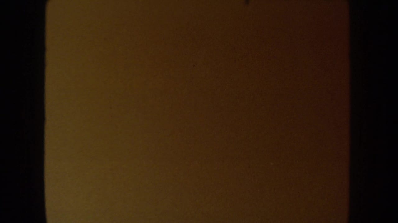 A dark, warm-toned 8mm frame from the 1954 South Dakota wedding clip, likely leader or underexposed transition footage.