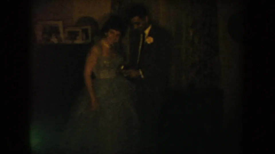 In a dim South Dakota wedding interior, a woman in a light gown stands near a man in a dark suit with a boutonniere.