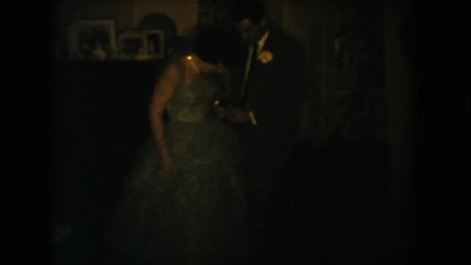 1954 South Dakota home-movie frame showing a couple in formal attire, partly obscured by low light and film grain.