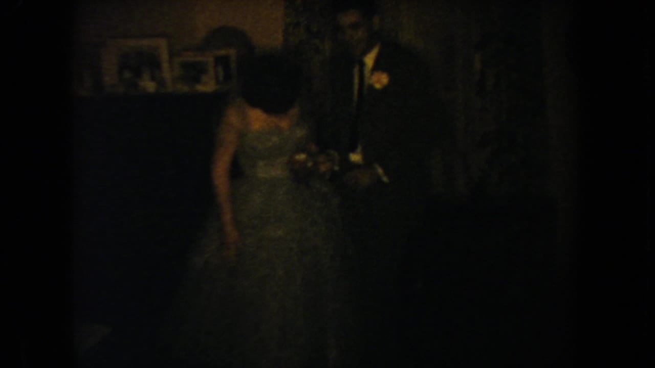 Woman in a light gown looks downward while a suited man stands beside her.