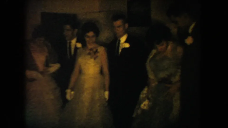 South Dakota 1954 wedding reception frame showing guests in formal clothing clustered in a dim room with warm 8mm color.