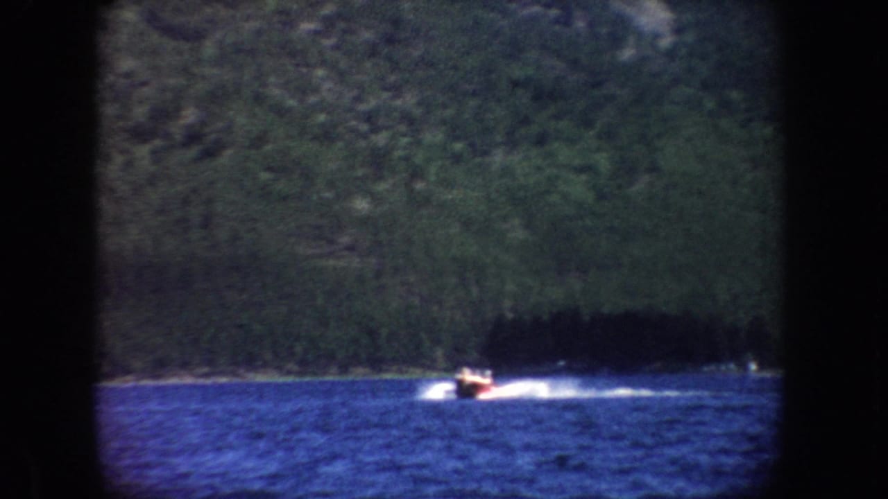 Motorboat throws spray while moving across open water near a tree-lined shore.