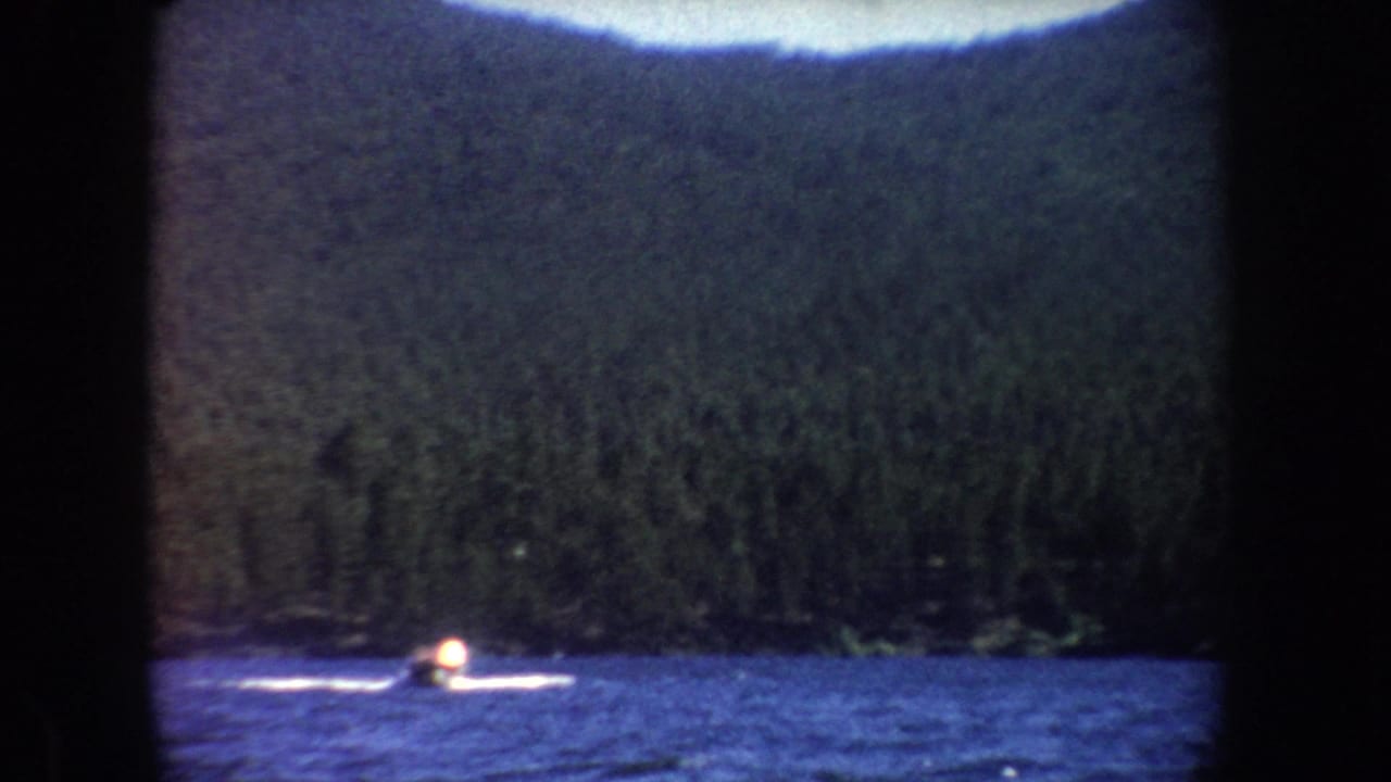 Soft 8mm frame of a small motorboat farther across the lake, with a white wake against dark shoreline trees.