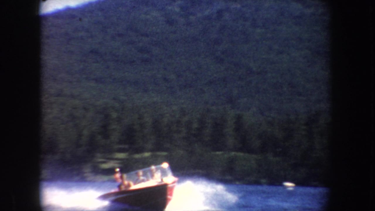 Closer 1954 home-movie view of a red and white motorboat with distant occupants, speeding across a South Dakota lake.
