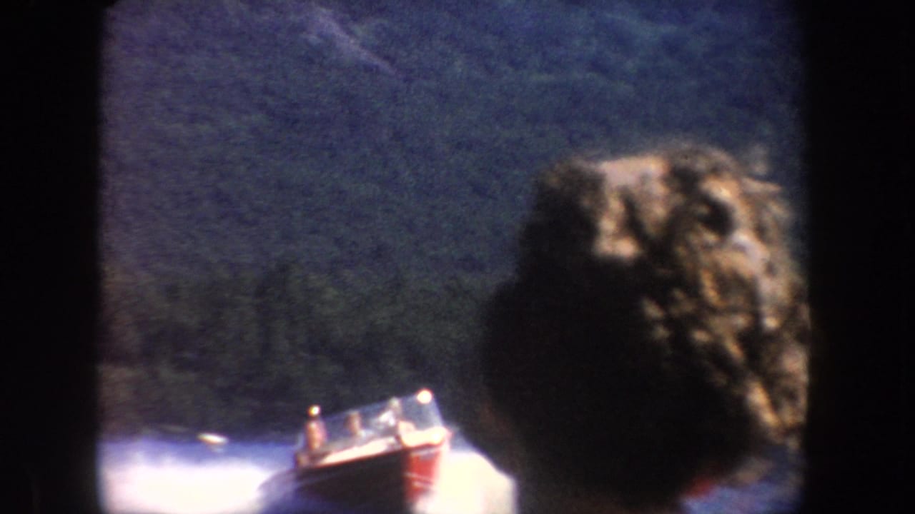 1954 South Dakota 8mm frame showing a red speedboat on a lake, partly obscured by a foreground passenger and dark film borders.