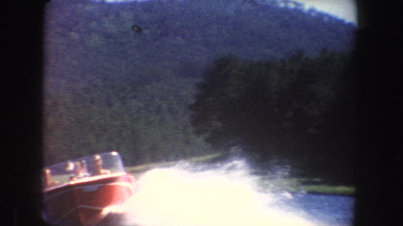 Red speedboat throwing white spray across a lake below wooded hills.
