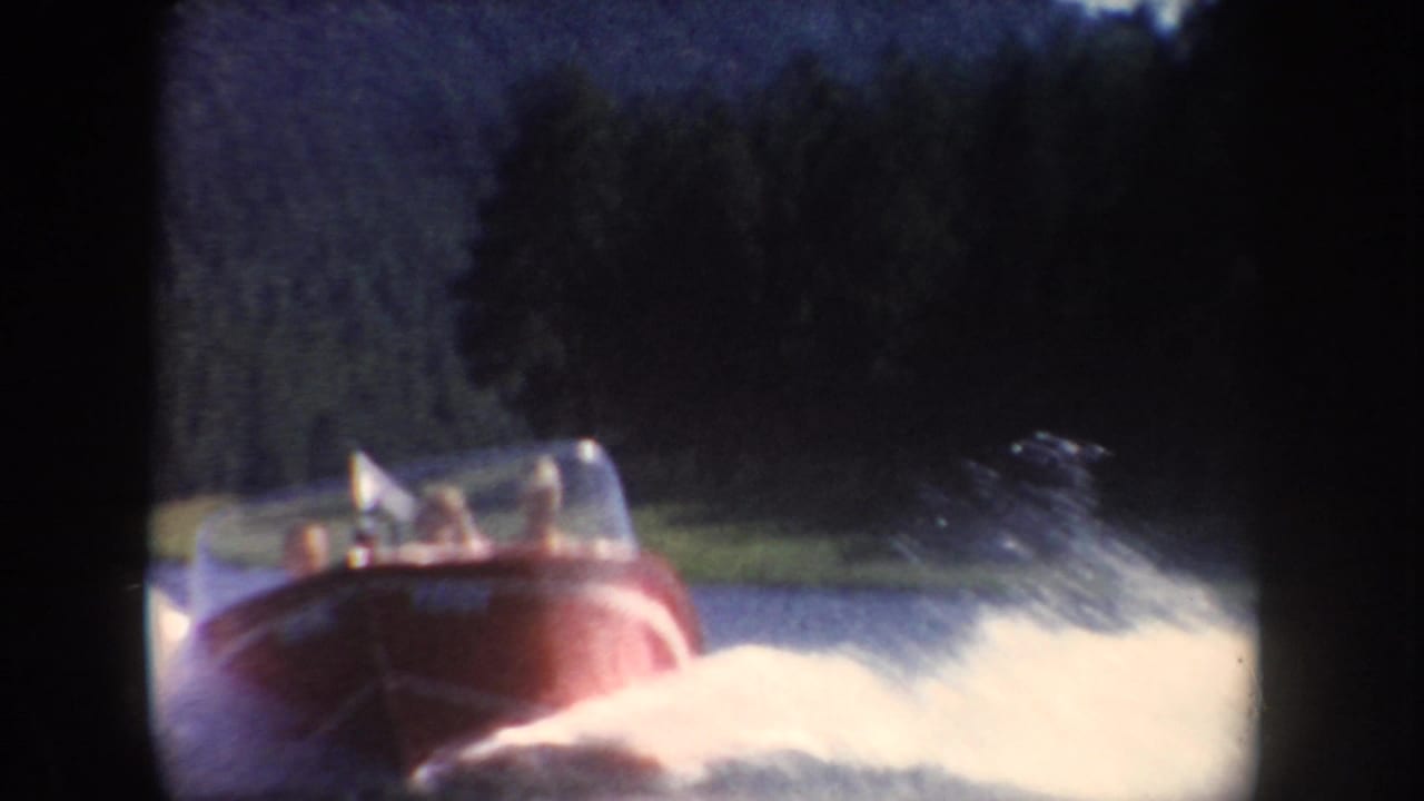 Close 8mm view of a red speedboat on a South Dakota lake, with seated passengers and water spray filling the lower frame.
