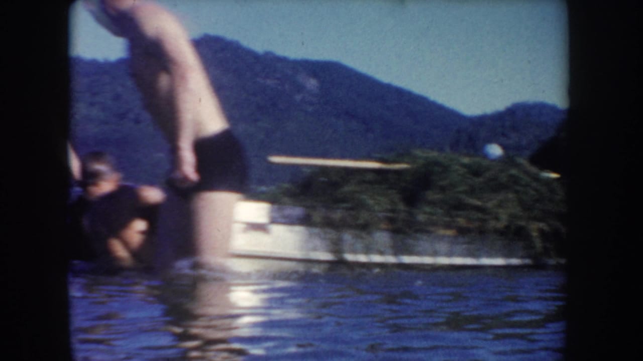 Adults stand in shallow lake water near a small boat, with wooded mountains behind them in the supplied South Dakota vacation footage.