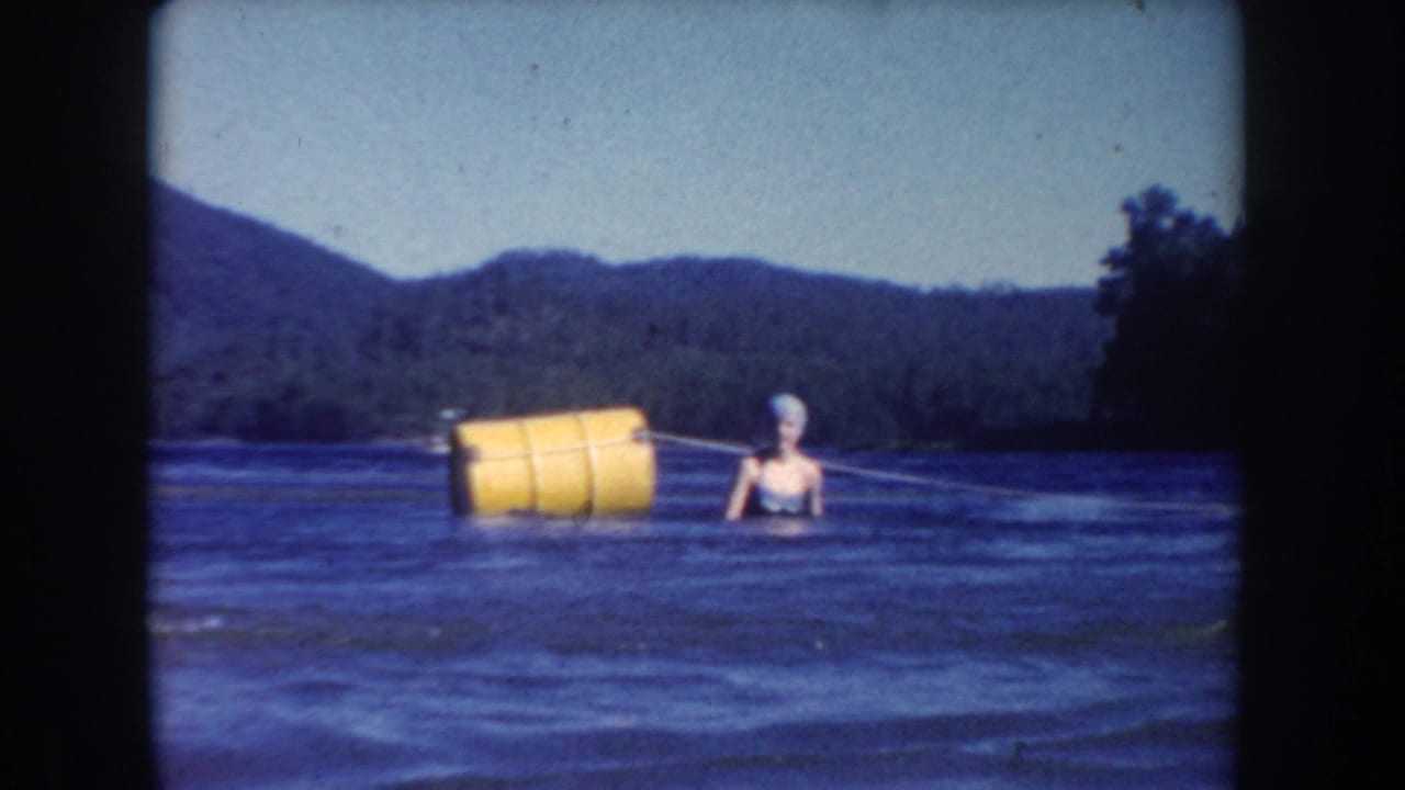 Woman in swim cap swimming near a large yellow buoy in open lake water.