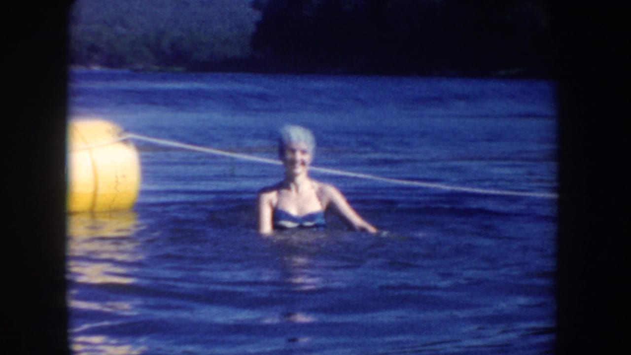 Adult woman in a swim cap smiles while standing in South Dakota lake water near a yellow buoy and rope line.