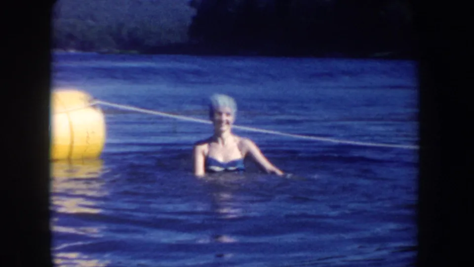 Adult woman in a swim cap smiles while standing in South Dakota lake water near a yellow buoy and rope line.
