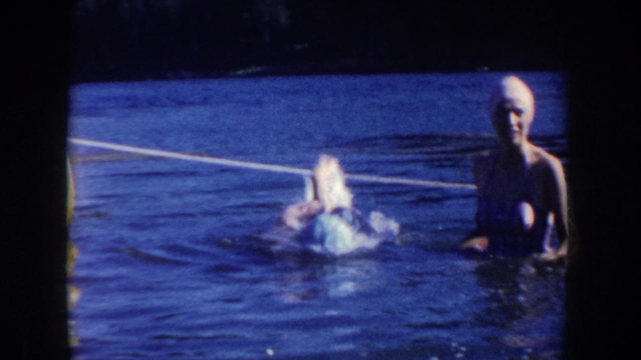 Two women in swim caps are in lake water as one splashes near a white swim rope.