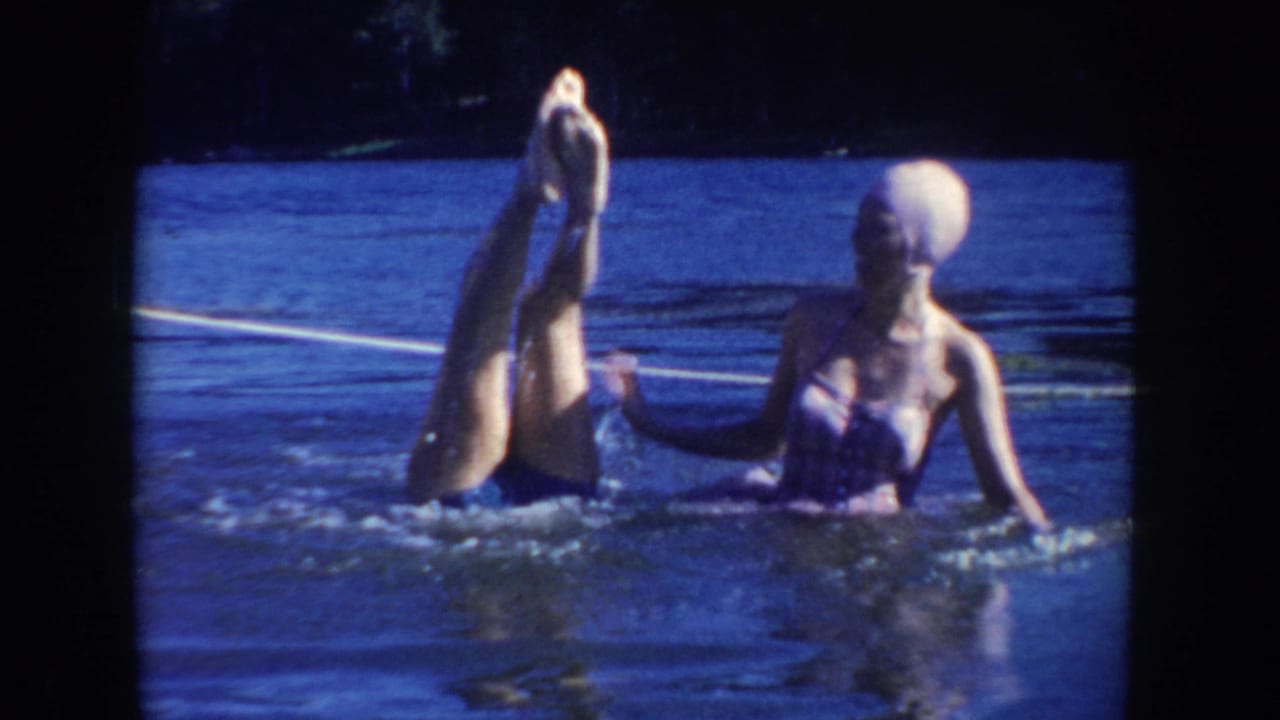 1954 South Dakota lake scene with one woman upside down in the water while another woman in a light swim cap steadies her nearby.