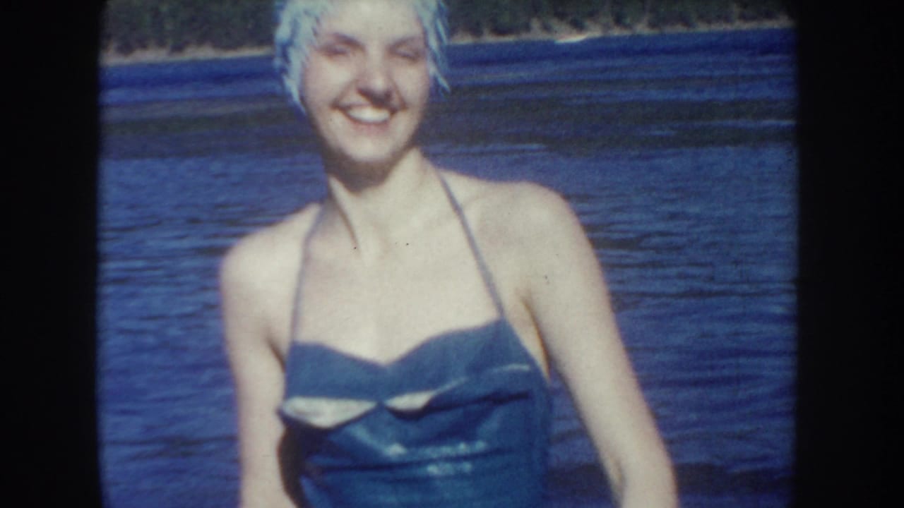 1954 South Dakota frame showing a smiling woman in a swim cap and one-piece swimsuit standing close to the camera in lake water.