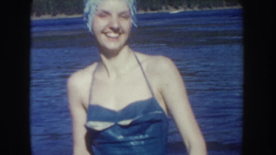 1954 South Dakota frame showing a smiling woman in a swim cap and one-piece swimsuit standing close to the camera in lake water.
