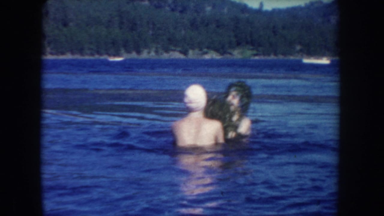 In 1954 South Dakota home-movie footage, two young women stand chest-deep in a lake while one playfully adds aquatic plants to the other's head.