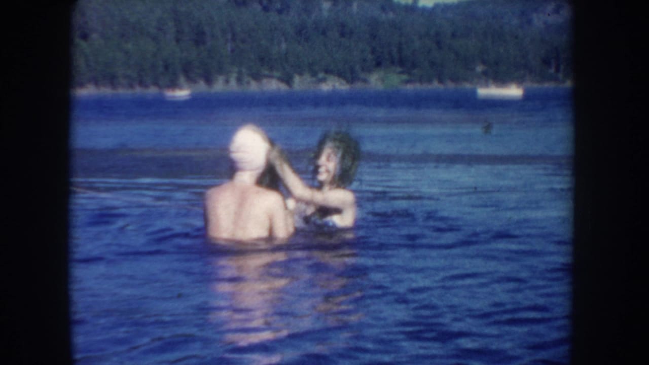 A young woman in a white swim cap faces away in a South Dakota lake while another swimmer raises wet aquatic plants toward her head.