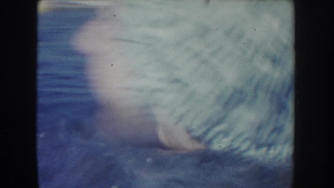 Soft 1954 South Dakota 8mm frame showing a swimmer close to the camera in lake water, with motion blur and dark film borders.