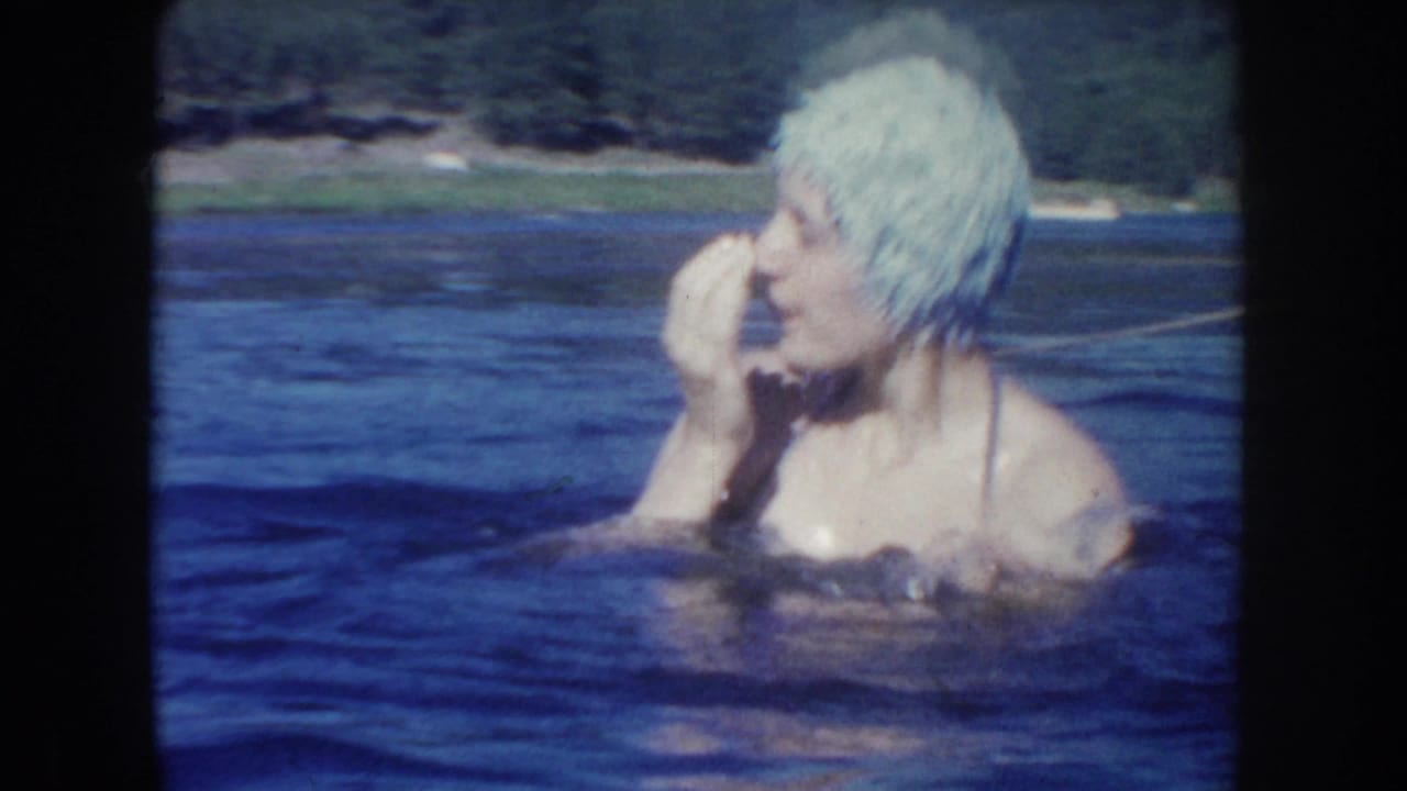 In 1954 South Dakota home-movie footage, a woman in a pale bathing cap reacts while standing chest-deep in lake water.