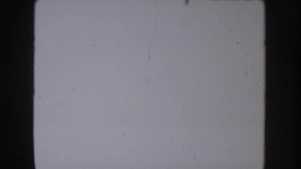 A pale, scratched 8mm frame from the clip opening, bordered by dark gate edges with no distinct person or landscape visible.
