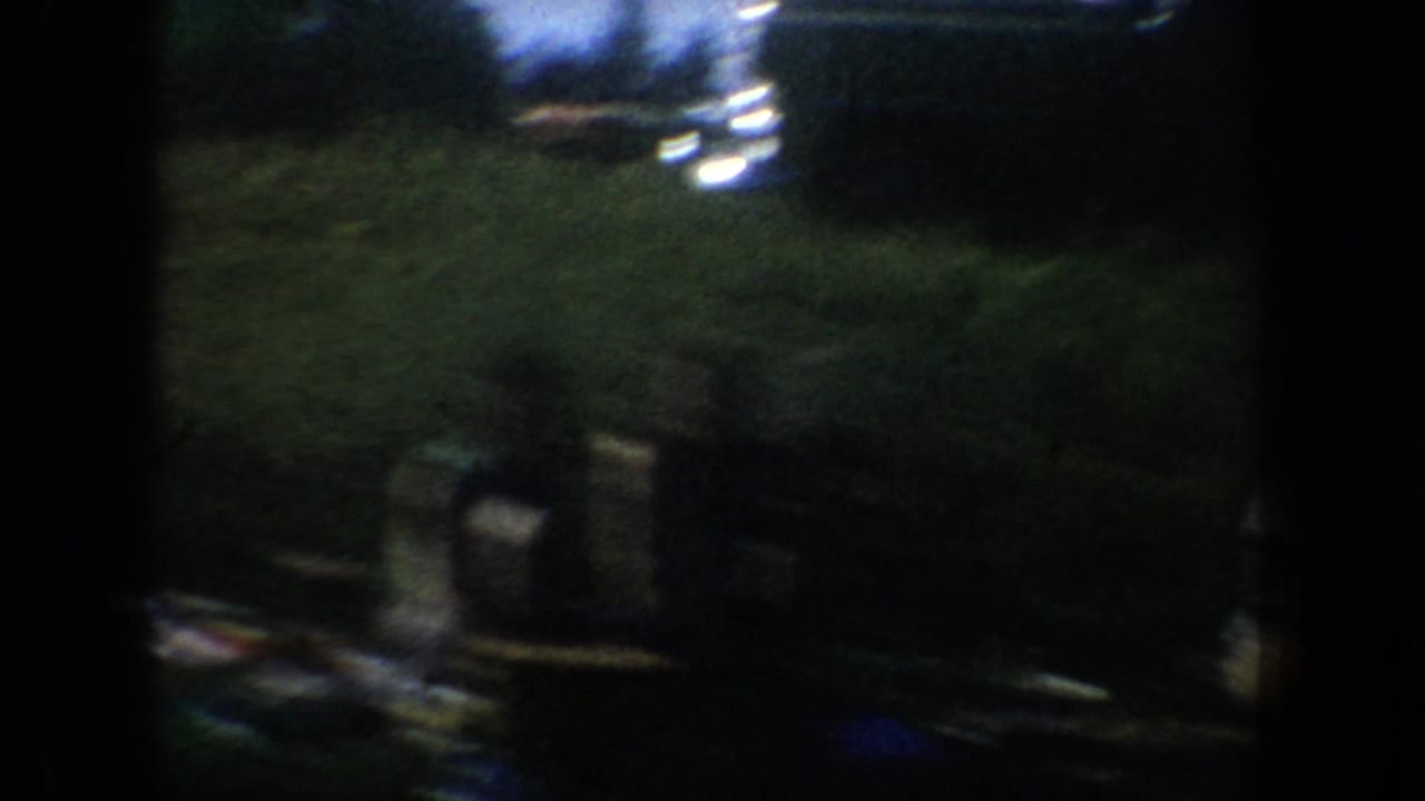 Low-light 1954 South Dakota 8mm frame showing an indistinct classroom or lecture interior with dark silhouettes and film edge shadow.