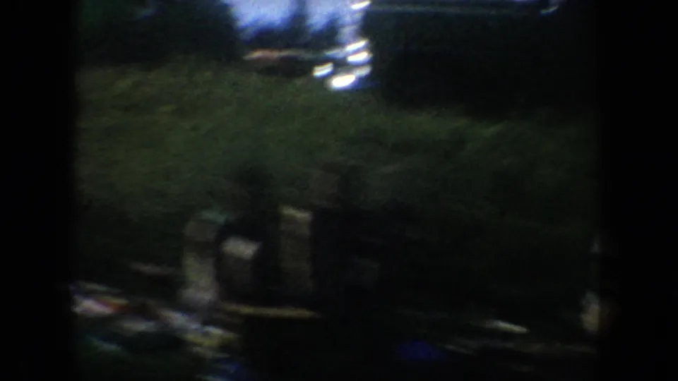 Low-light 1954 South Dakota 8mm frame showing an indistinct classroom or lecture interior with dark silhouettes and film edge shadow.