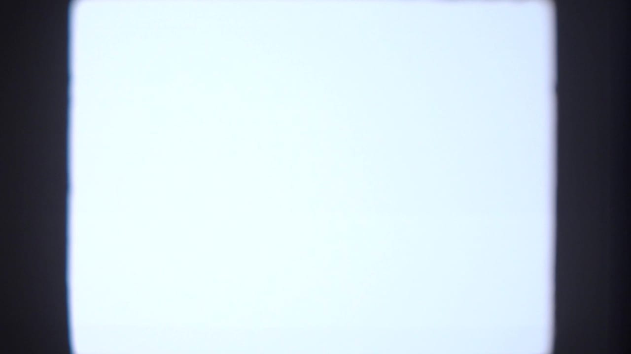 Blank bright projection screen or illuminated surface in the 1954 South Dakota classroom footage, framed by dark edges.