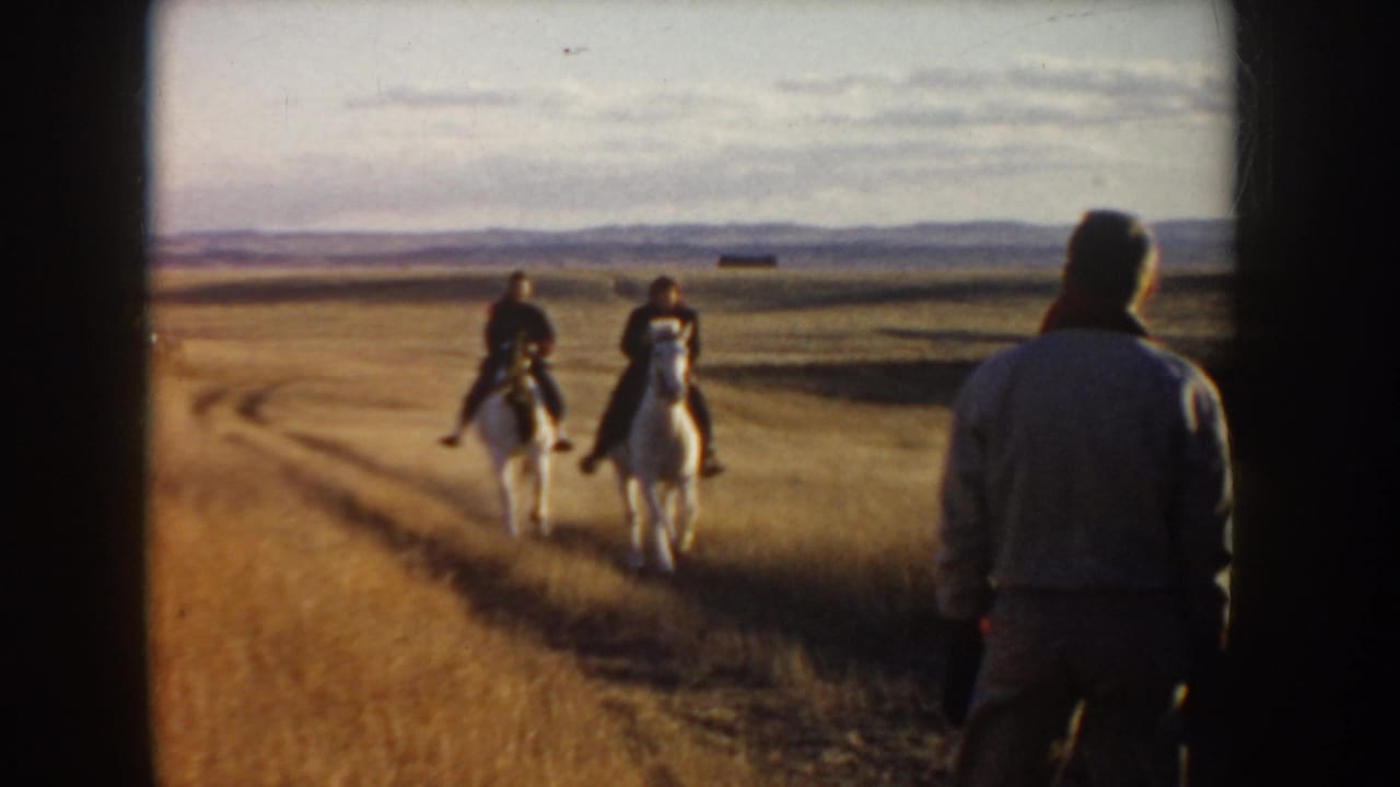 In rural Idaho 1955 home-movie footage, a person stands in the foreground as two riders on white horses continue down the road.