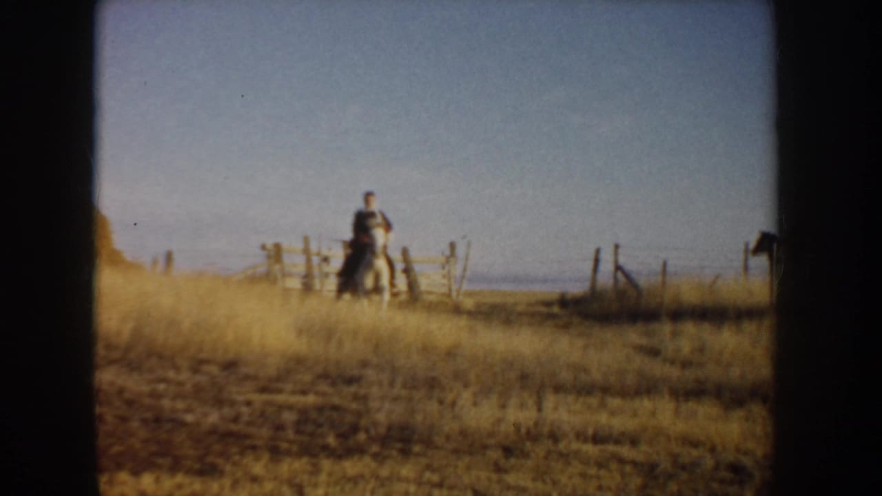 In 1955 Idaho home-movie footage, a distant rider moves near a wooden fence across dry open grassland.