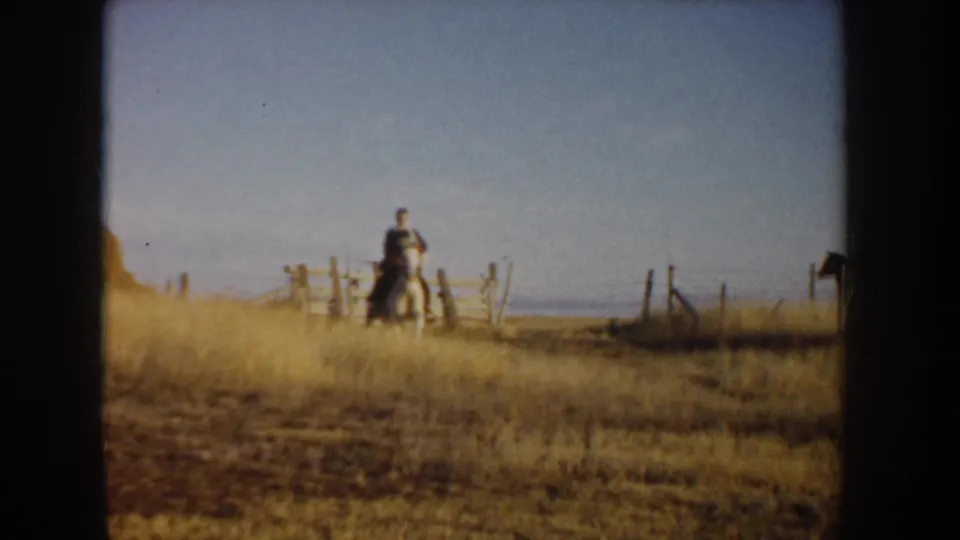 In 1955 Idaho home-movie footage, a distant rider moves near a wooden fence across dry open grassland.