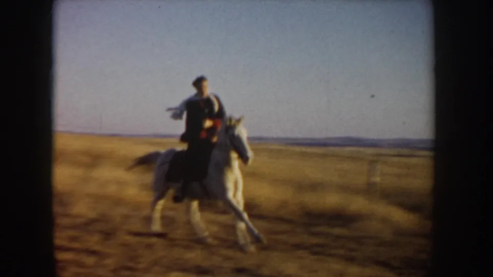 A rider on a light-colored horse crosses open grassland in soft, handheld 8mm footage from Idaho.