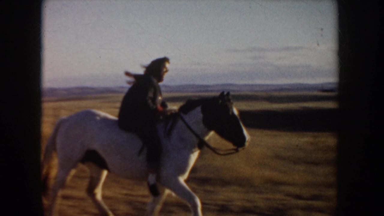 1955 Idaho home-movie frame of a rider in dark clothing on a black-and-white horse moving across open prairie at low sun.