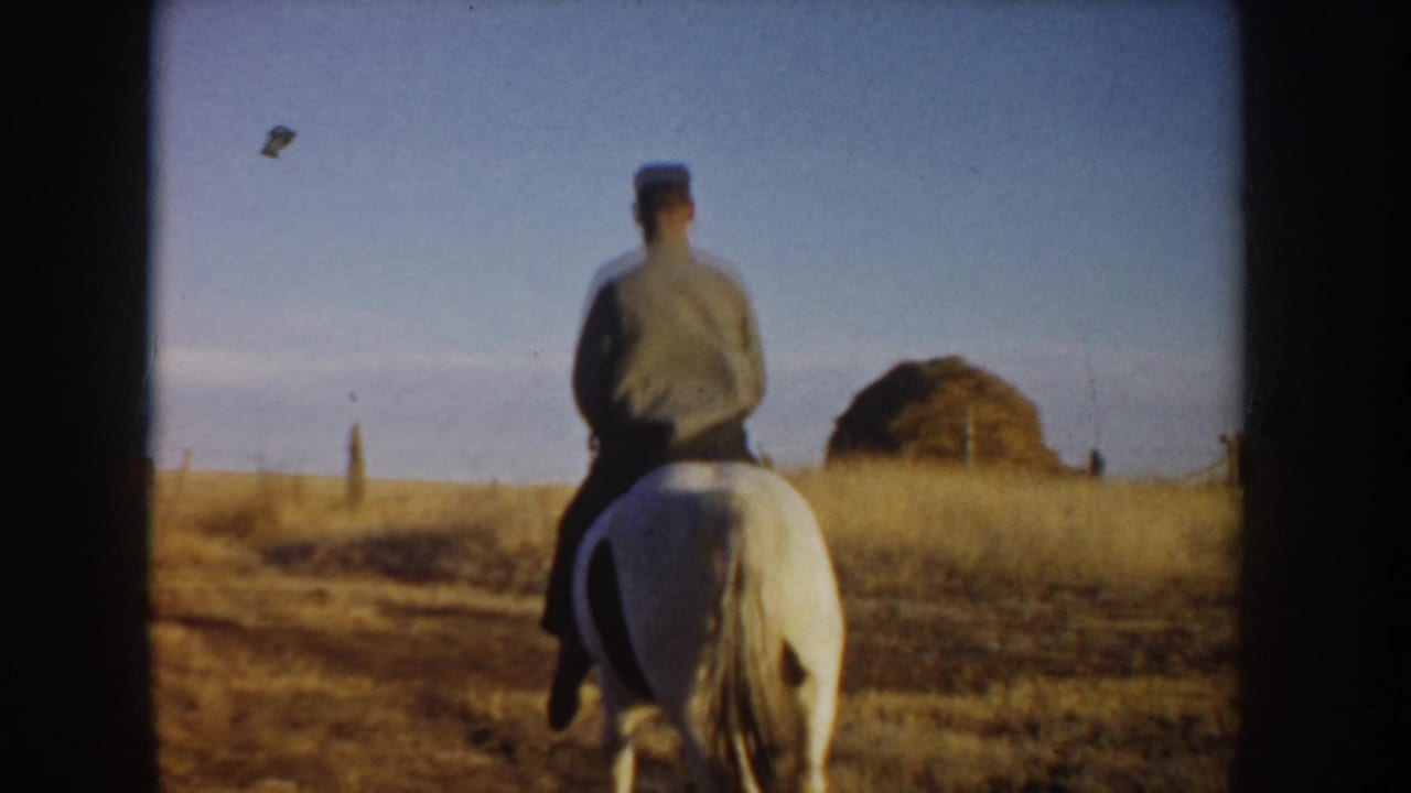 In 1955 Idaho home-movie footage, a man rides a white horse away from the camera through a dry rural field.