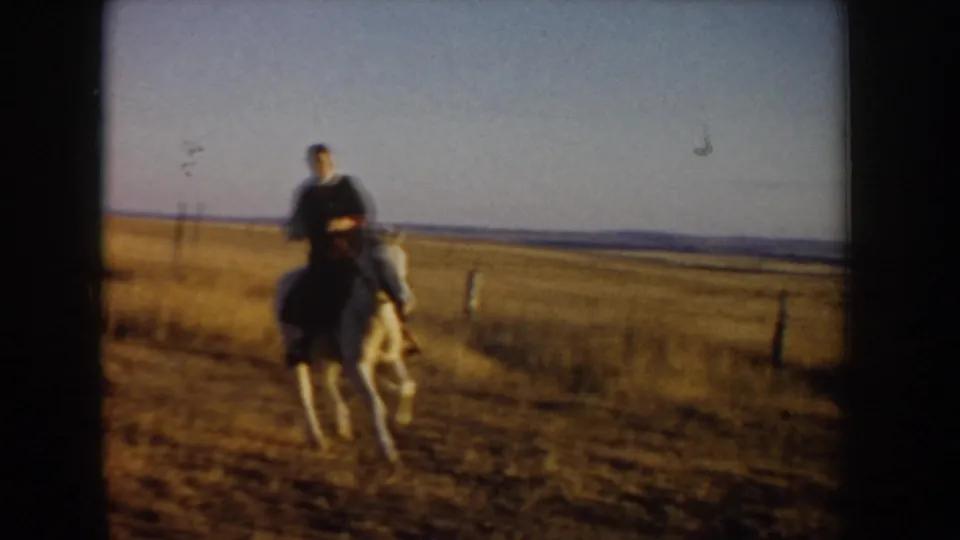 A horseback rider moves toward the camera across an Idaho field, with fence posts and low hills beyond.