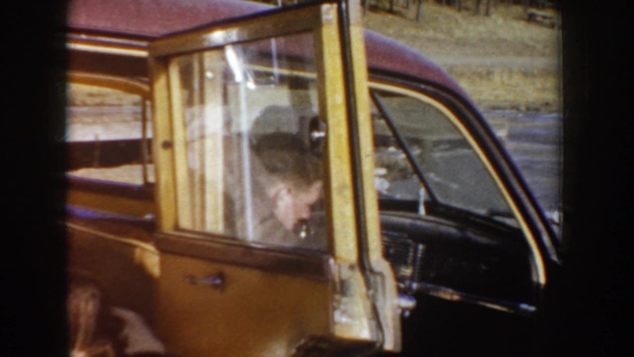 1955 Idaho 8mm frame showing an open yellow car door and a partially visible passenger inside a mid-century vehicle.
