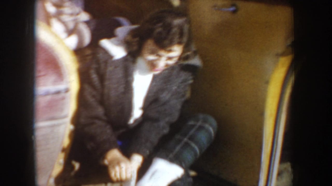 Young woman seated inside a car, leaning forward near a rounded seat back.