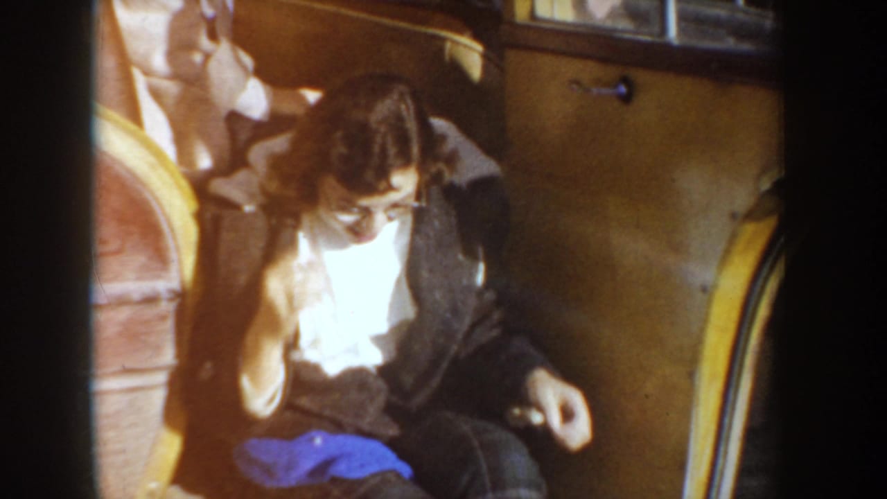 1955 Idaho home-movie frame showing a person in glasses and a dark coat preparing near the camera before ice skating.