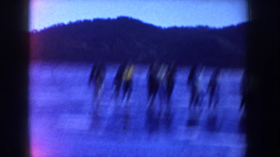 Motion-blurred 1955 Idaho home-movie frame of skaters crossing a frozen lake in winter clothing.