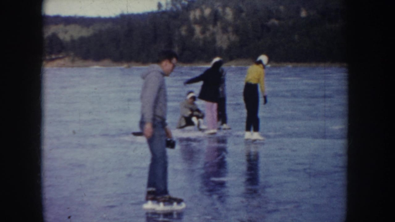 A small group of skaters stands and glides on reflective lake ice.
