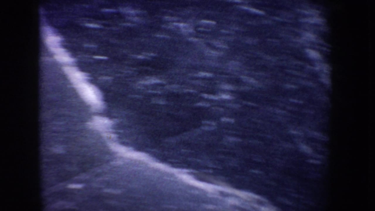 1955 Idaho 8mm frame showing abstract blue ice texture on a frozen lake, with soft focus and heavy film grain.