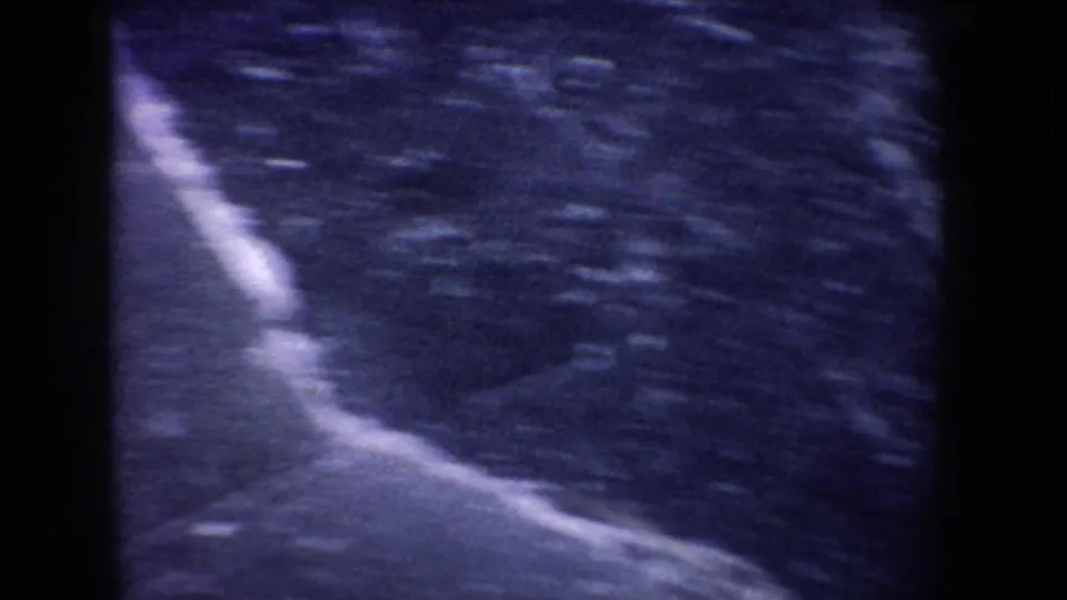 1955 Idaho 8mm frame showing abstract blue ice texture on a frozen lake, with soft focus and heavy film grain.