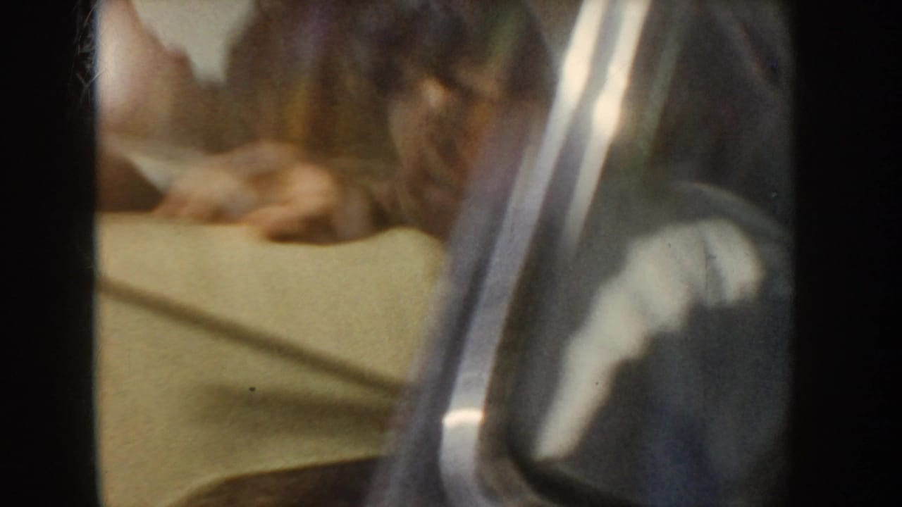 1955 Idaho 8mm frame showing a close, reflected view inside a car with pale vinyl upholstery and a partially visible person.